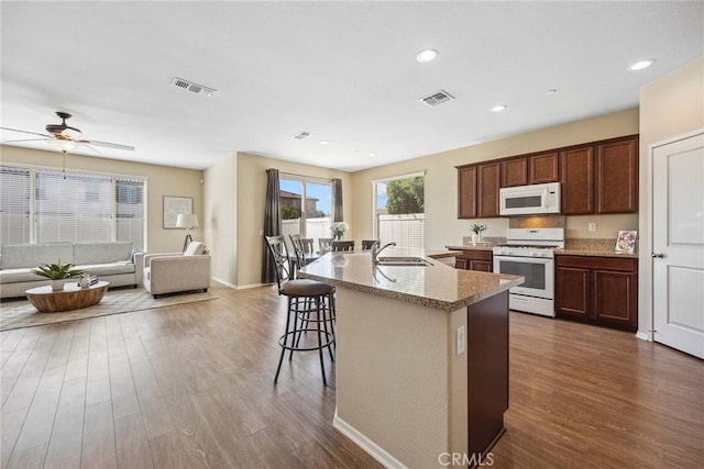 kitchen featuring dark hardwood / wood-style flooring, white appliances, ceiling fan, a kitchen island with sink, and sink