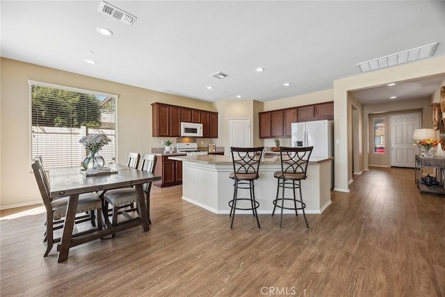 kitchen featuring a center island, a kitchen breakfast bar, light stone counters, white appliances, and hardwood / wood-style flooring