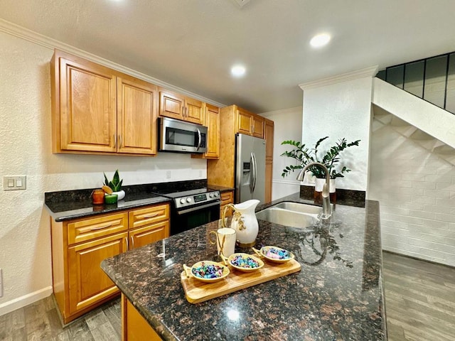 kitchen featuring appliances with stainless steel finishes, dark stone counters, light hardwood / wood-style floors, sink, and ornamental molding