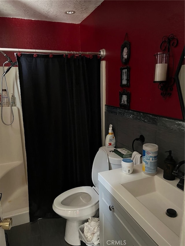 bathroom with toilet, tile walls, a shower with shower curtain, vanity, and a textured ceiling