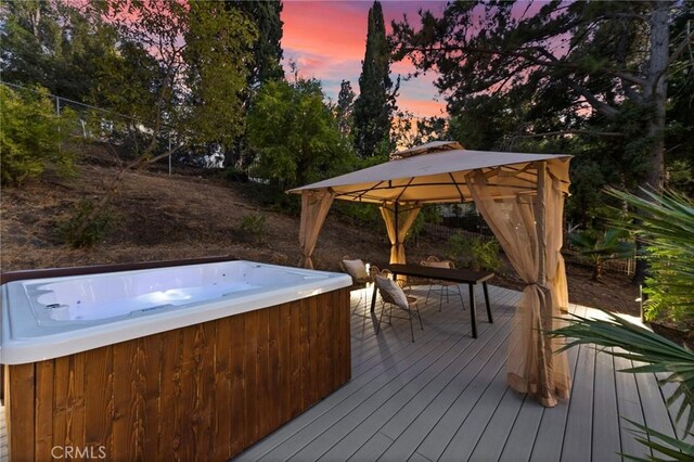 deck at dusk with a gazebo and a hot tub