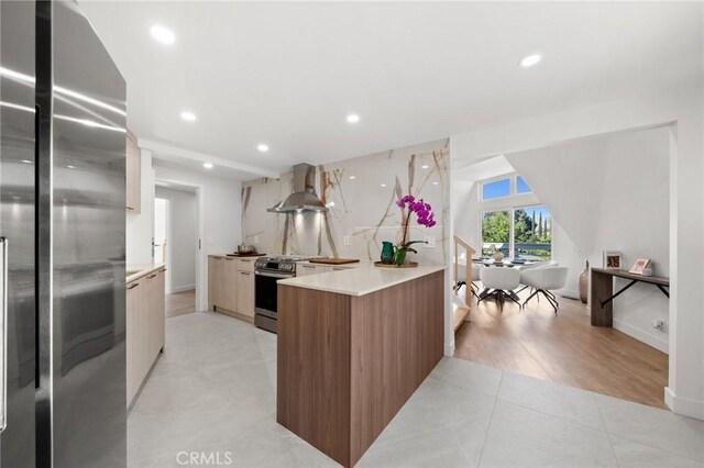 kitchen with wall chimney range hood, appliances with stainless steel finishes, and light tile patterned flooring