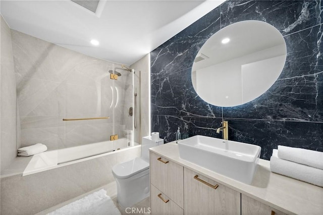 full bathroom featuring toilet, tiled shower / bath combo, tile walls, and vanity