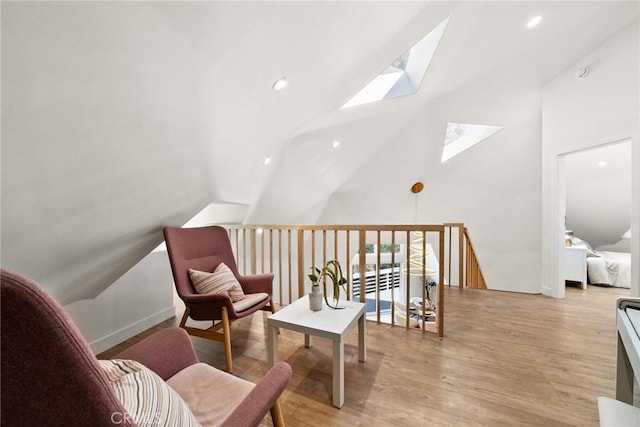 sitting room with vaulted ceiling with skylight and light wood-type flooring