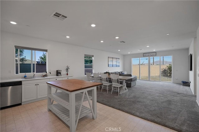 kitchen featuring sink, stainless steel dishwasher, white cabinets, and light colored carpet