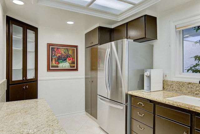 kitchen featuring crown molding, light stone countertops, stainless steel refrigerator, sink, and dark brown cabinets