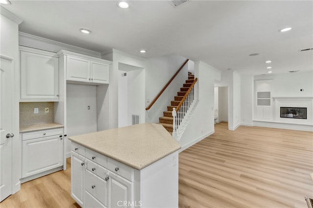 kitchen with light wood-type flooring, a center island, tasteful backsplash, white cabinets, and crown molding