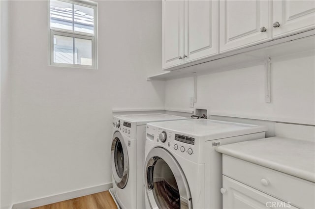 clothes washing area with cabinets, light hardwood / wood-style floors, and washing machine and clothes dryer