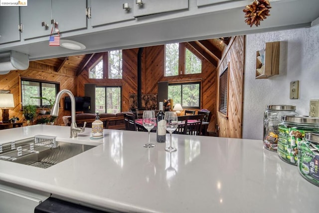 kitchen with lofted ceiling with beams, wooden walls, and sink