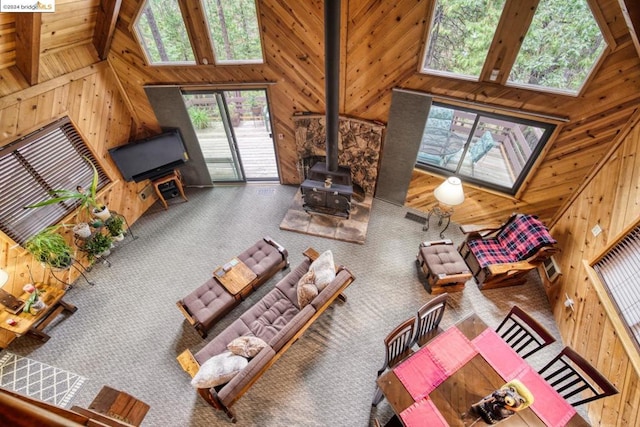 carpeted living room featuring wood walls, beam ceiling, a wood stove, and high vaulted ceiling