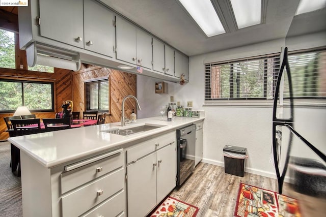 kitchen featuring black dishwasher, wooden walls, sink, and a wealth of natural light