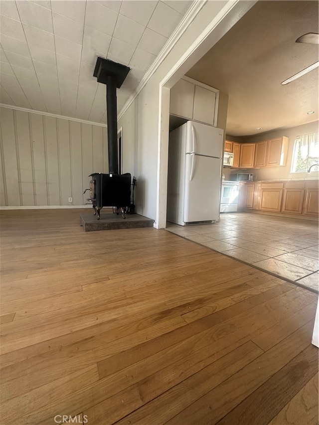 unfurnished living room with crown molding, light hardwood / wood-style floors, ceiling fan, and a wood stove