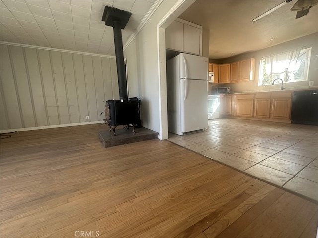 unfurnished living room featuring ceiling fan, sink, a wood stove, light hardwood / wood-style flooring, and crown molding