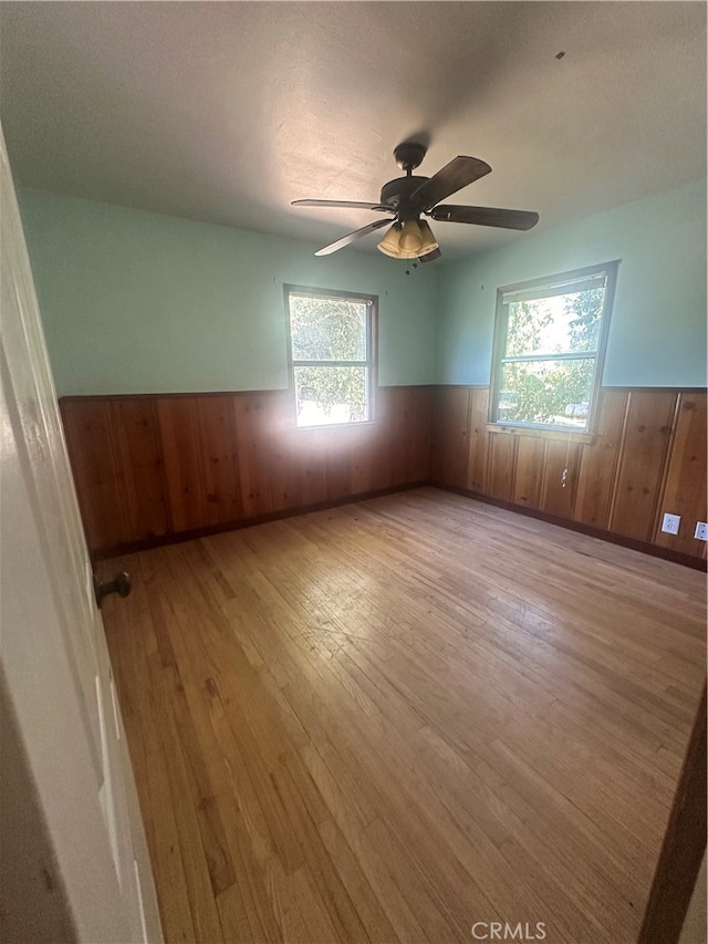 empty room with light hardwood / wood-style floors, wood walls, and plenty of natural light