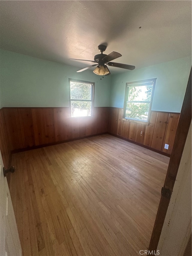 spare room with light wood-type flooring, a textured ceiling, wood walls, and ceiling fan