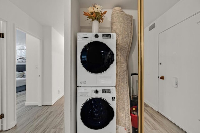 laundry room with light hardwood / wood-style floors and stacked washer / drying machine