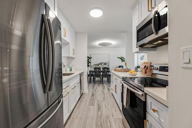 kitchen featuring white cabinetry, light hardwood / wood-style floors, appliances with stainless steel finishes, light stone counters, and sink