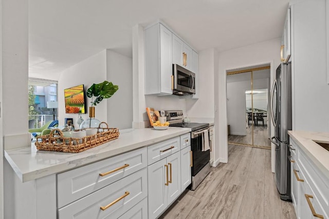 kitchen with light hardwood / wood-style floors, kitchen peninsula, stainless steel appliances, light stone countertops, and white cabinets