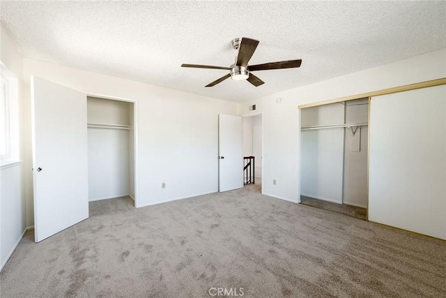 unfurnished bedroom featuring carpet flooring, two closets, a textured ceiling, and ceiling fan