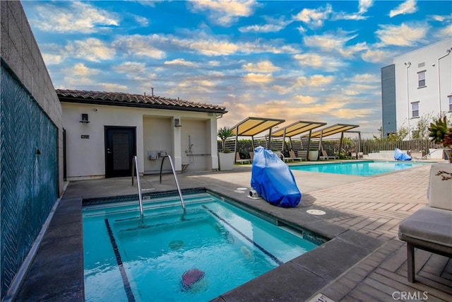 pool at dusk featuring a patio and a hot tub