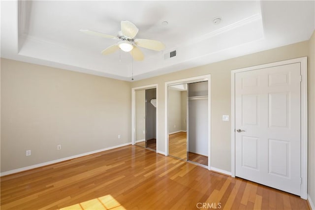 unfurnished bedroom with hardwood / wood-style flooring, ceiling fan, a raised ceiling, and two closets