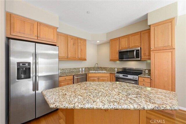 kitchen with sink, a kitchen island, light stone countertops, light hardwood / wood-style floors, and stainless steel appliances