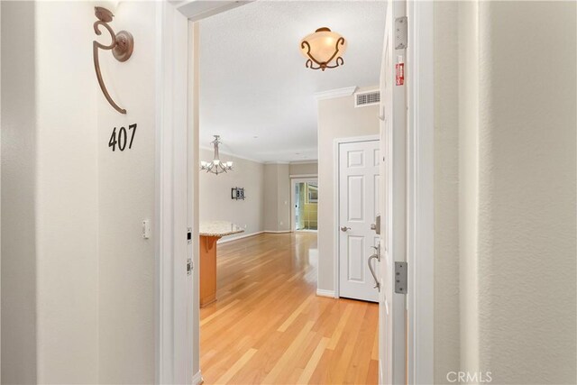 corridor featuring ornamental molding, a notable chandelier, and light wood-type flooring