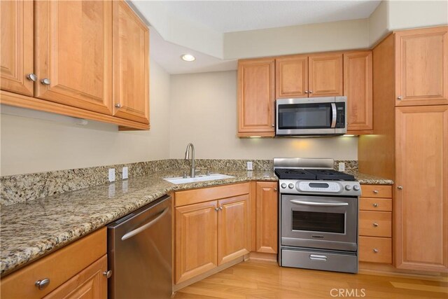 kitchen featuring light stone countertops, stainless steel appliances, light hardwood / wood-style floors, and sink