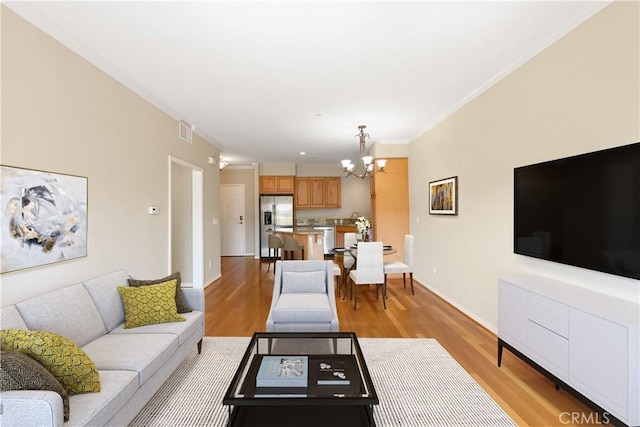 living room featuring crown molding, an inviting chandelier, and light wood-type flooring