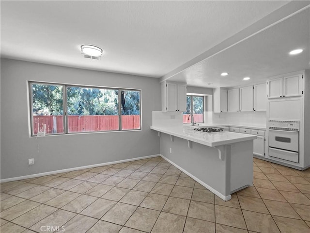 kitchen featuring light tile patterned floors, kitchen peninsula, white appliances, and white cabinetry