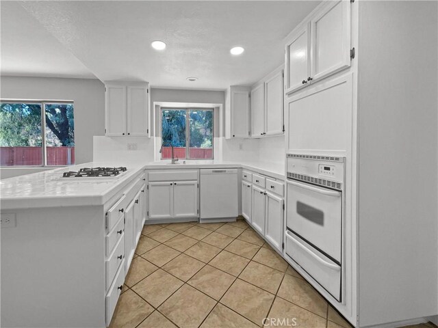 kitchen with white cabinetry, white appliances, light tile patterned floors, and kitchen peninsula