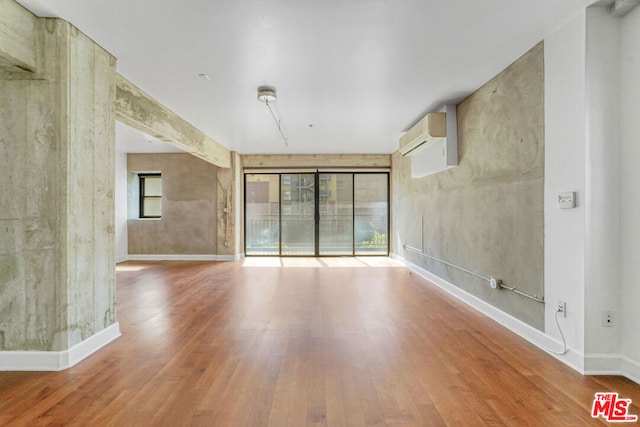 empty room featuring wood-type flooring, a healthy amount of sunlight, and a wall mounted AC