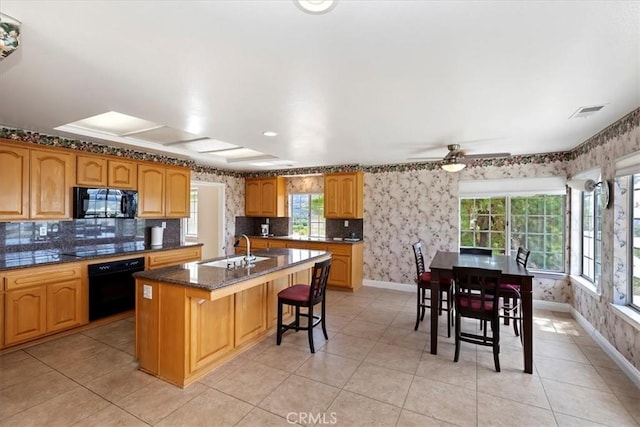 kitchen with sink, light tile patterned flooring, oven, and a center island with sink