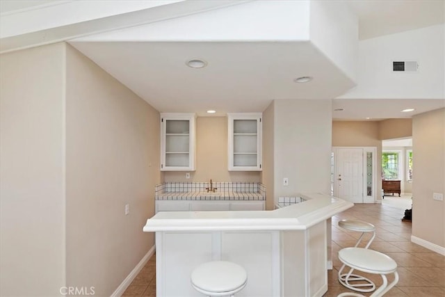 kitchen featuring white cabinets, vaulted ceiling, a kitchen breakfast bar, and light tile patterned floors