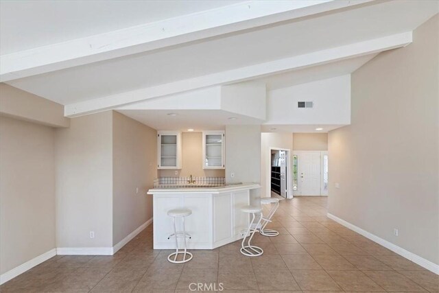 kitchen featuring a breakfast bar, vaulted ceiling with beams, sink, white cabinetry, and light tile patterned floors