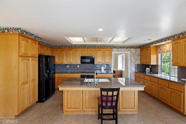 kitchen with black appliances, a kitchen bar, sink, light tile patterned flooring, and an island with sink