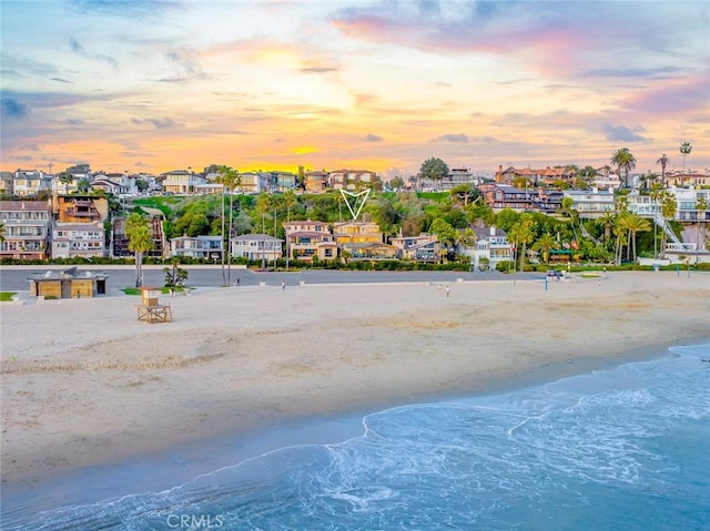 aerial view at dusk featuring a view of the beach and a water view