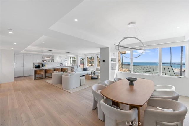 dining area with a water view, plenty of natural light, a raised ceiling, and light hardwood / wood-style floors