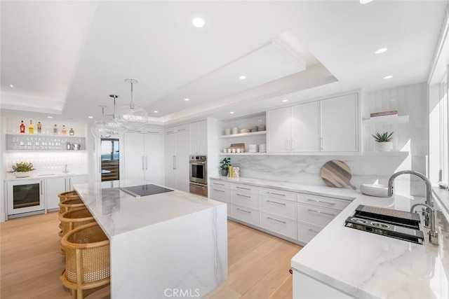 kitchen with a raised ceiling, white cabinetry, a kitchen island, and stainless steel oven