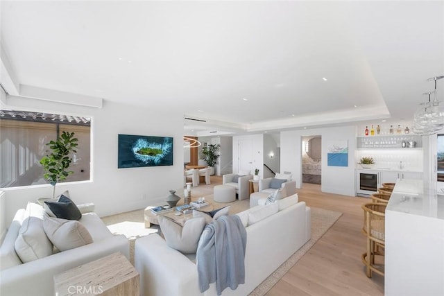 living room featuring bar, beverage cooler, a raised ceiling, and light hardwood / wood-style floors