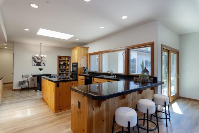 kitchen featuring sink, a skylight, a center island, black appliances, and light wood-type flooring