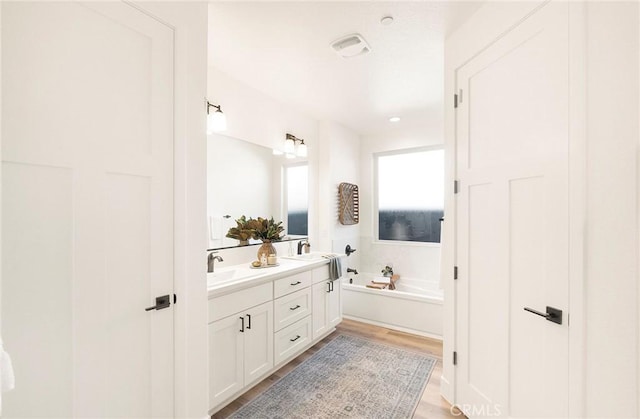 bathroom with hardwood / wood-style flooring, vanity, and a tub to relax in