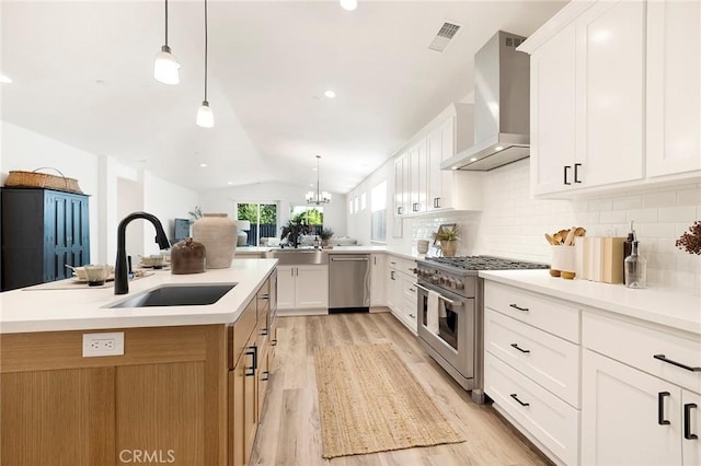 kitchen with white cabinets, wall chimney exhaust hood, stainless steel appliances, and vaulted ceiling