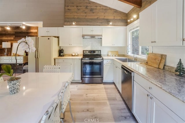 kitchen featuring appliances with stainless steel finishes, white cabinetry, light hardwood / wood-style flooring, vaulted ceiling with beams, and sink