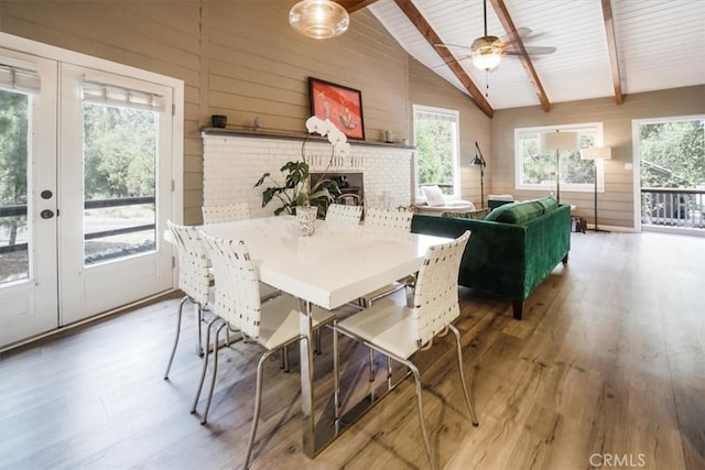 dining room featuring french doors, vaulted ceiling with beams, hardwood / wood-style flooring, and a fireplace