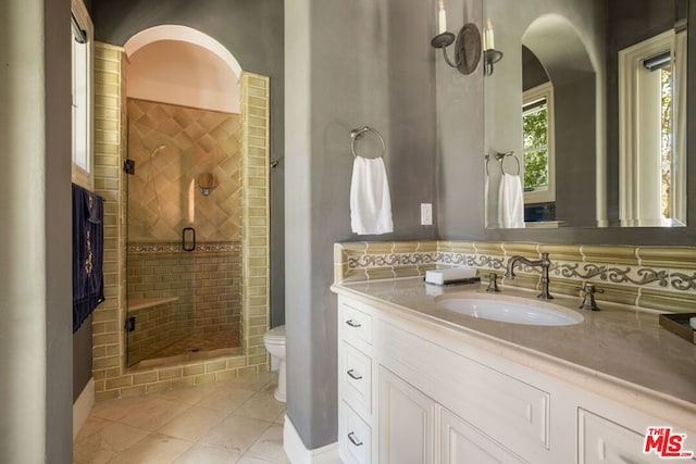 bathroom featuring tile patterned floors, toilet, decorative backsplash, a shower with door, and vanity