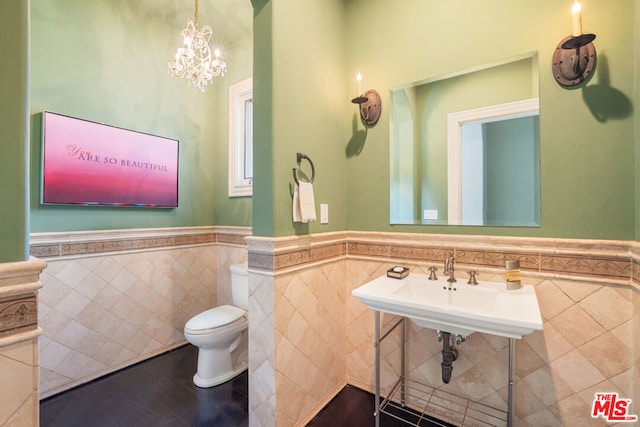 bathroom with toilet, tile walls, a notable chandelier, and sink