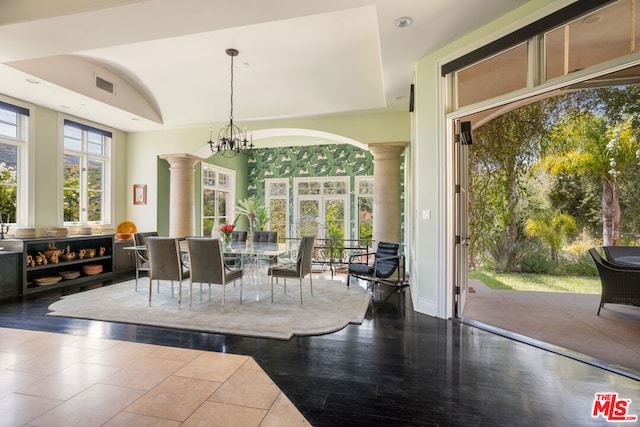 dining area with a notable chandelier, a raised ceiling, and ornate columns