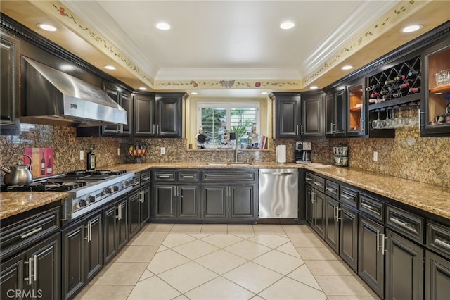 kitchen with appliances with stainless steel finishes, wall chimney exhaust hood, ornamental molding, and a tray ceiling