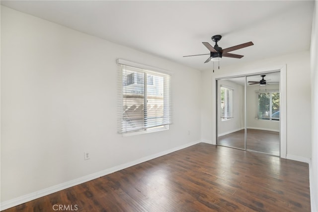 unfurnished bedroom featuring multiple windows, dark hardwood / wood-style flooring, ceiling fan, and a closet